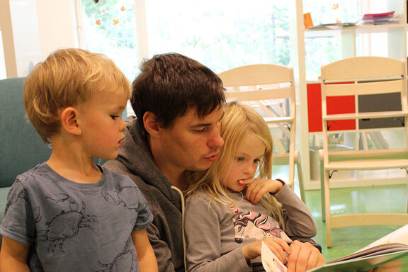 Mann som les for to barn i barnehagen til nettside